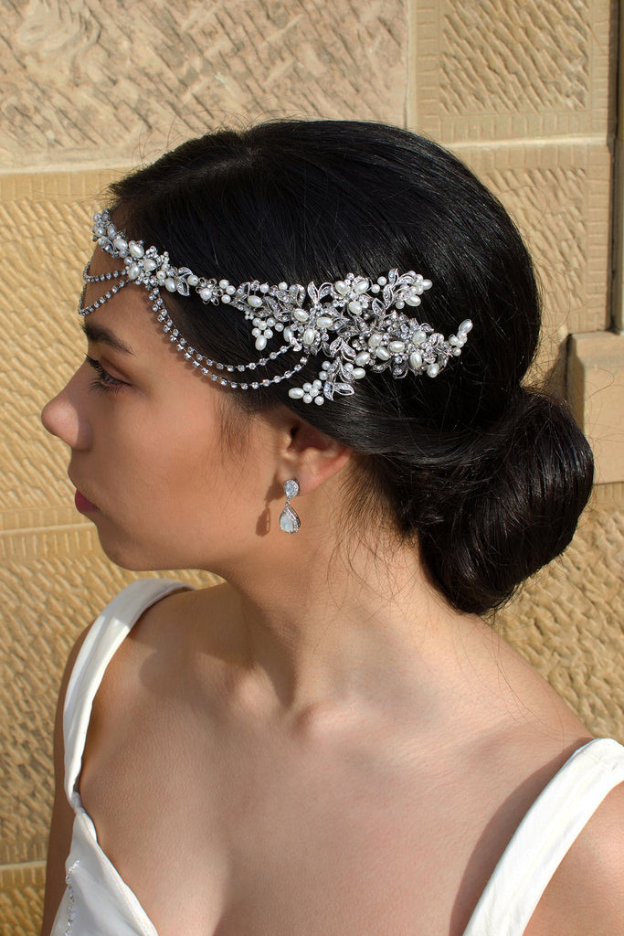 On the side of her head a bride wears a pearls and rhodium handmade vine with a stone wall backdrop
