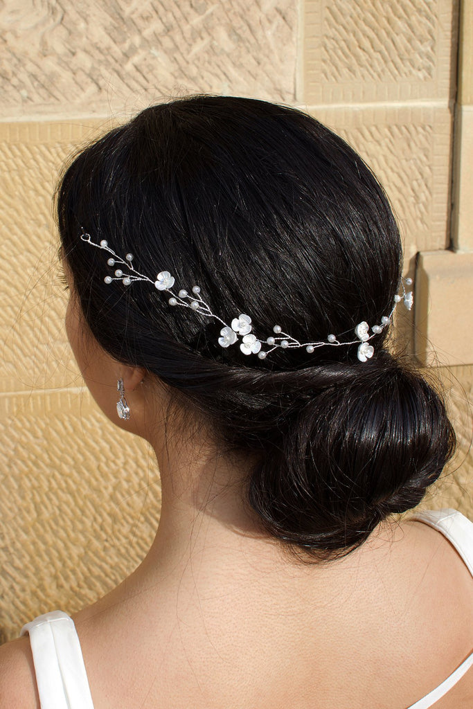 Thin wire bridal vine with pearls and small flowers on a black hair bride pictured in front of a stone wall