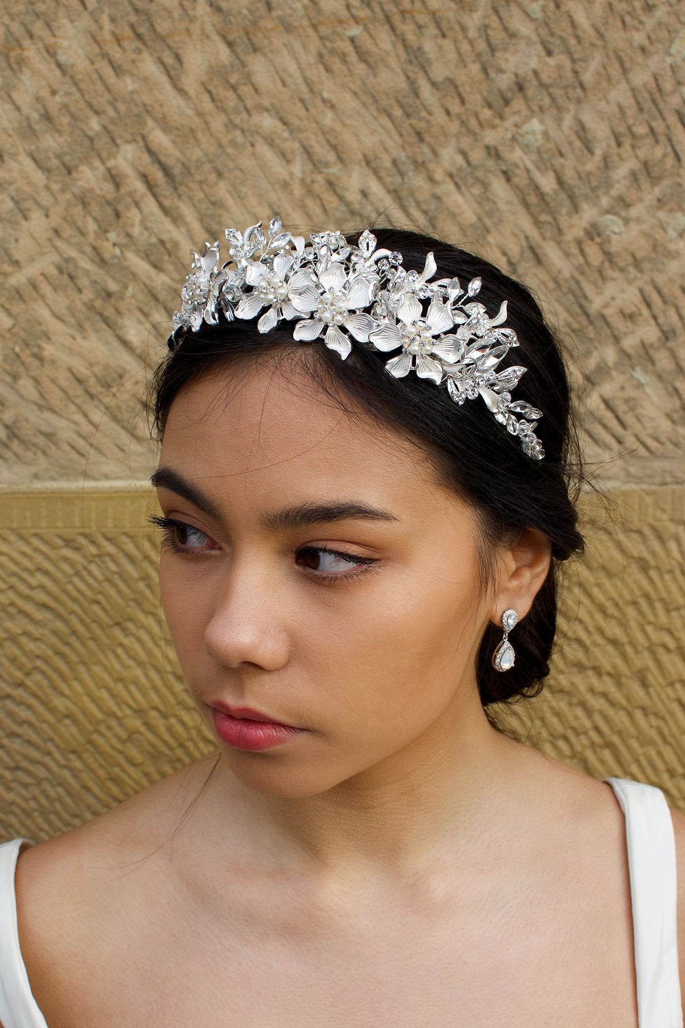 Soft Silver Handmade Tiara with leaves and pearl flowers on a dark hair model in front of an old sandstone wall