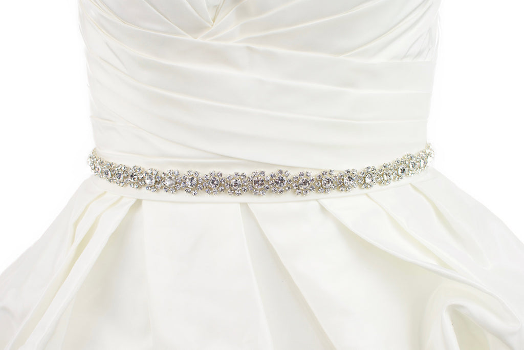 A narrow crystal bridal belt with rings of crystals around the pearls is worn on an ivory bridal gown