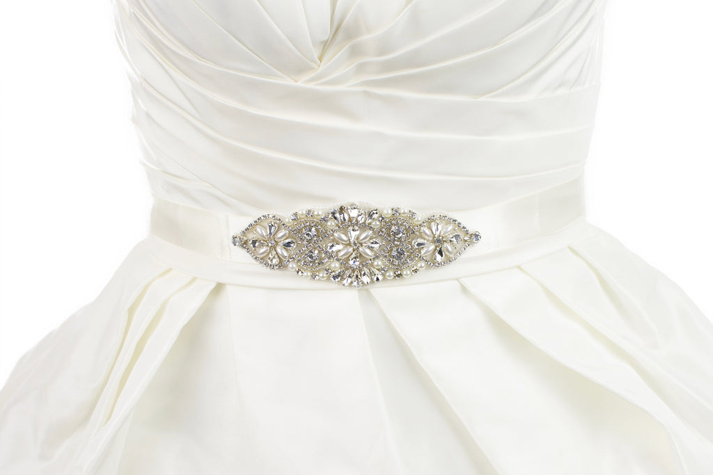 Small crystal and pearl bridal belt motif on an ivory ribbon worn on an ivory dress with white background