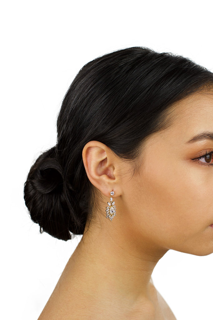 A short drop earring in gold is worn by a dark hair bridal model with a white background