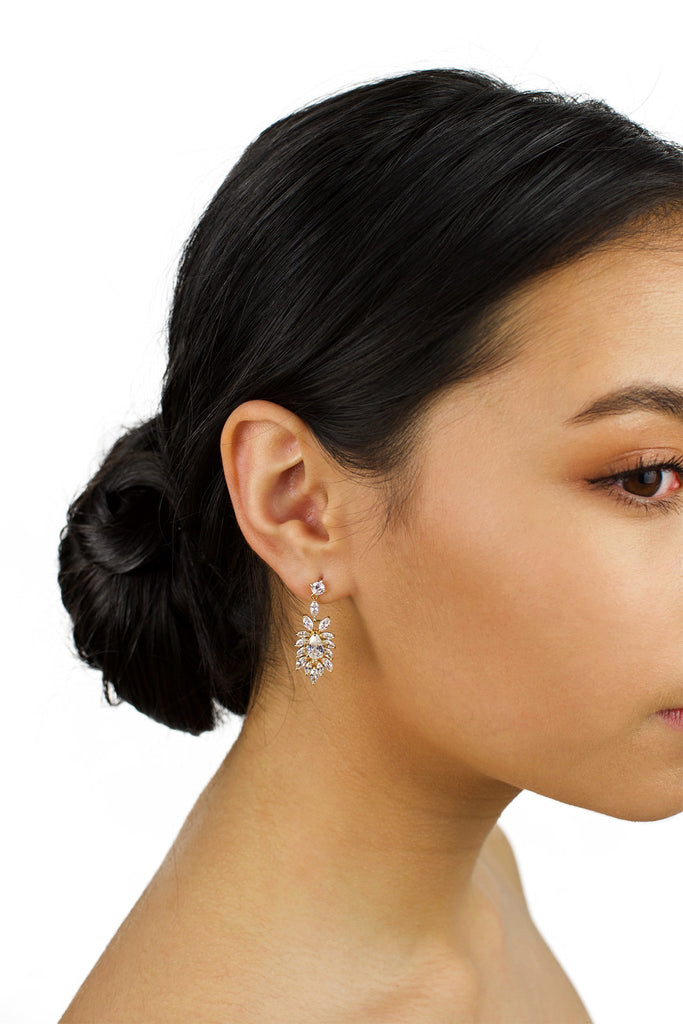 Model wears a gold drop earring in her ear with dark hair and a white background