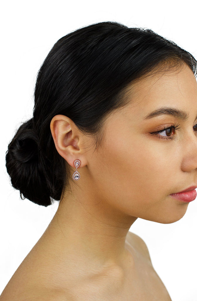 Small pear shape rose gold earring worn by a bridal model with dark hair on a white background