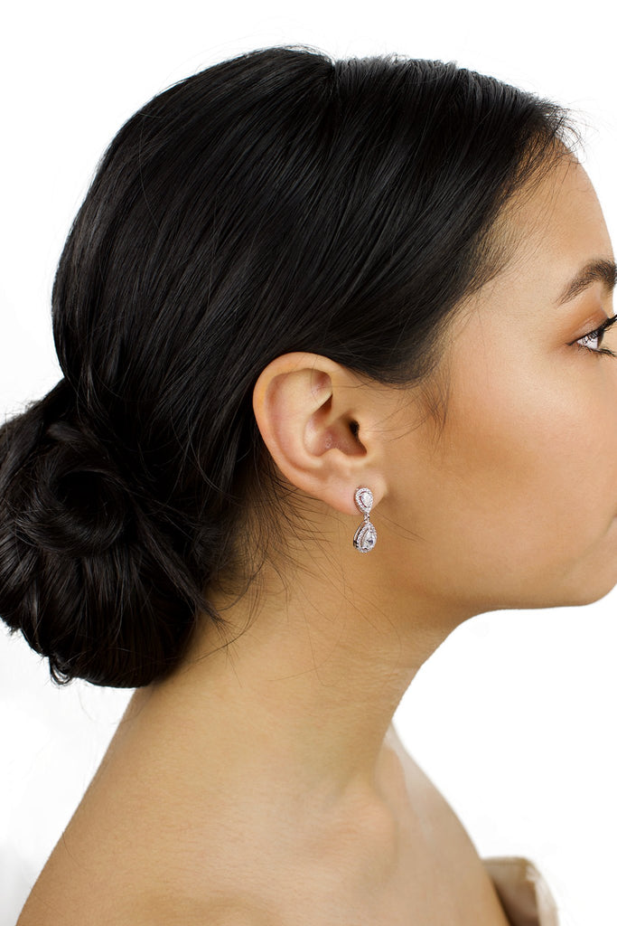 Small Silver pear shape earring worn by a bride with dark hair on a white background