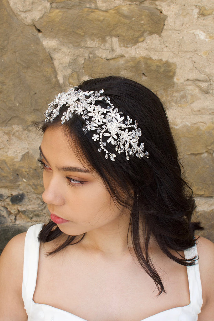 Side view of a bridal model wearing a wide crystal headband for brides with a stone wall backdrop