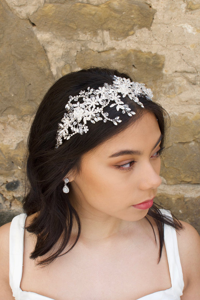 Model wears a silver crystal headband on her dark hair with a stone wall background
