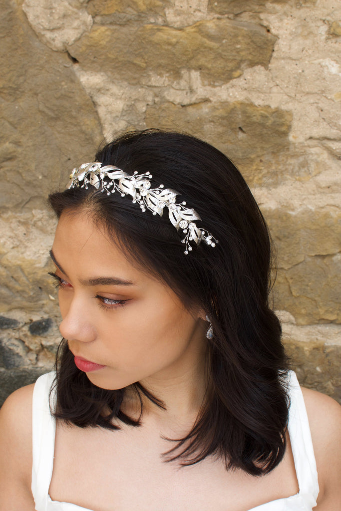 Looking to the left a model wears a beautiful silver bridal headband in her dark hair