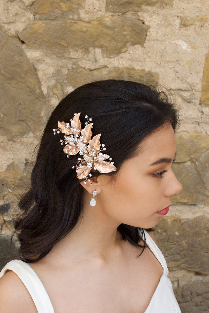 Rose Gold Leaves Side Comb with bright crystal sprigs worn by a dark hair model with a stone wall backdrop.