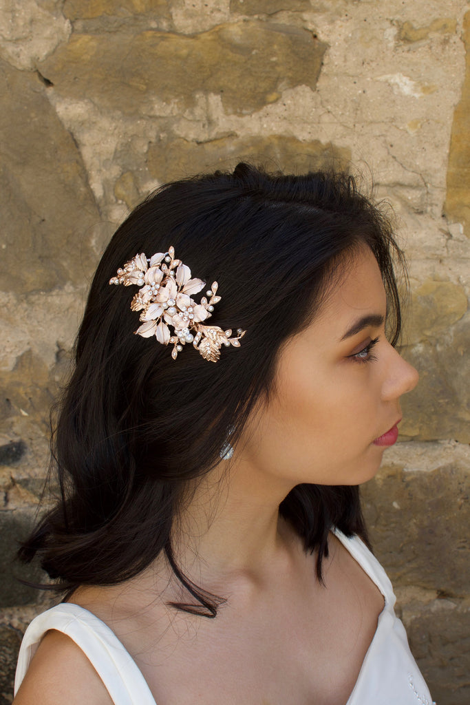 Pale Rose Gold Bridal Comb with leaves and flowers worn by a dark hair bride with a stone wall backdrop