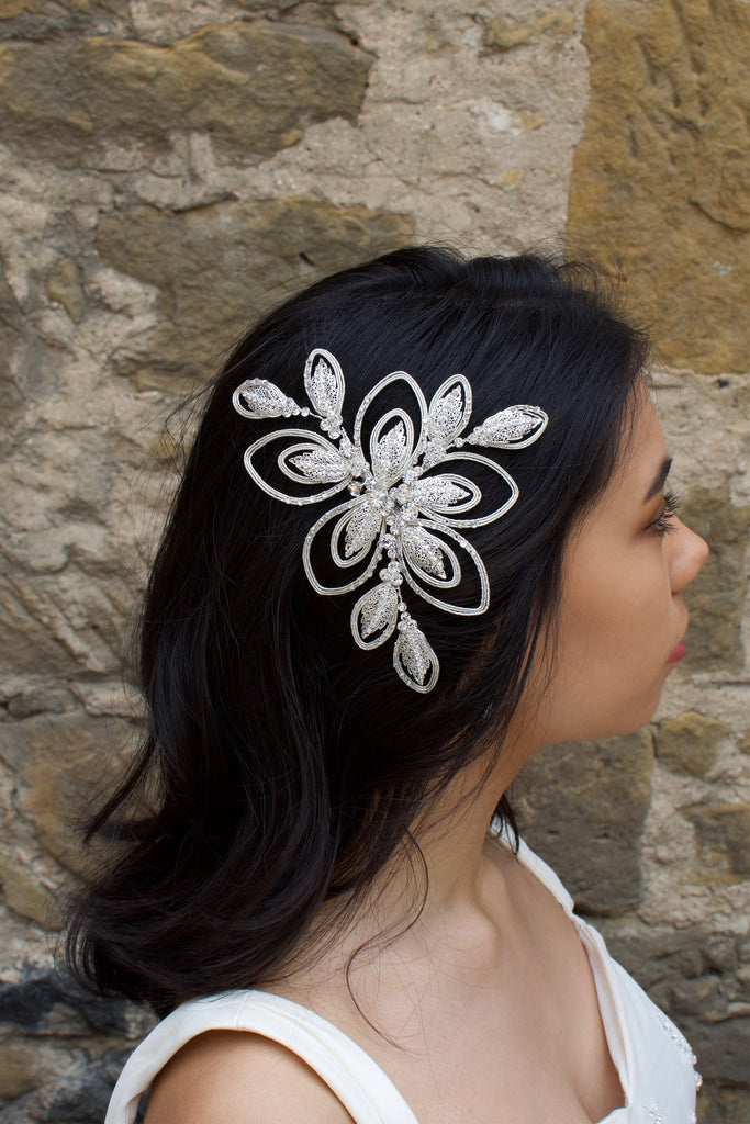 A dark haired bride wears a soft matt silver bridal side comb with a stone wall background