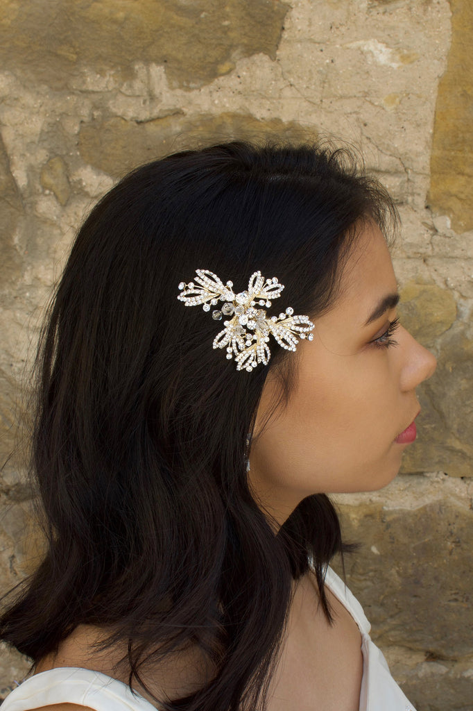 Model with dark hair wears a silver and flower side comb with a stone wall backdrop