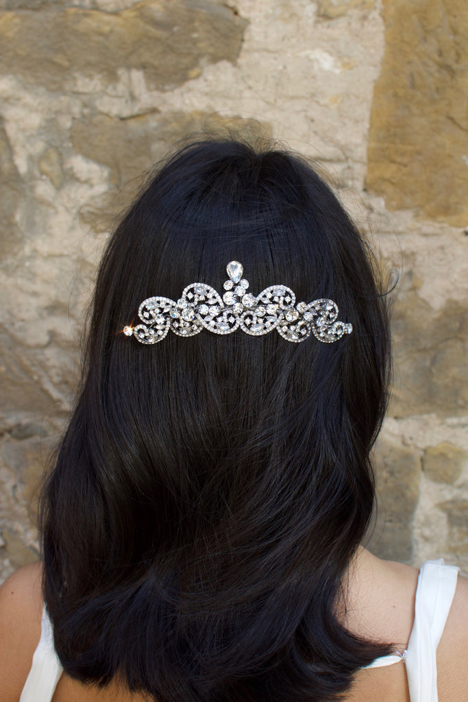 Model with long black hair wears a silver crystal comb at the back of her head in front of an old stone wall