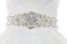 A wide bridal belt with crystals and beads worn on the waist of an ivory bridal gown with a white background