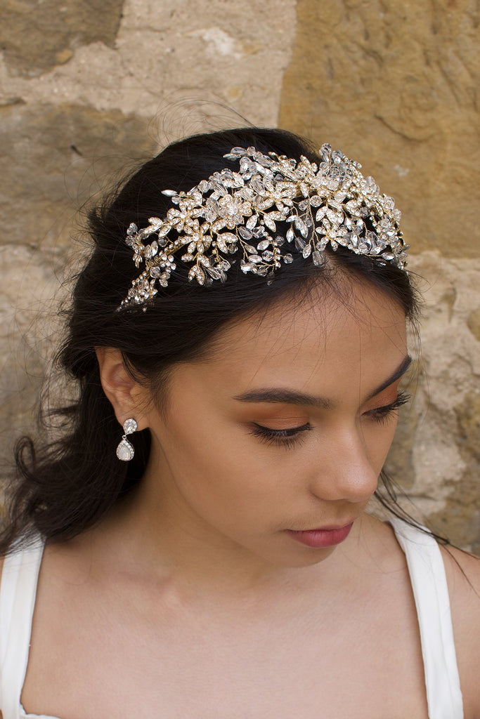 A model with dark hair wears a wide golden headband on the front of her head