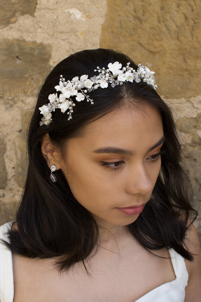 Dark hair model wears a headband of ceramic flowers  and pearls with a wall background