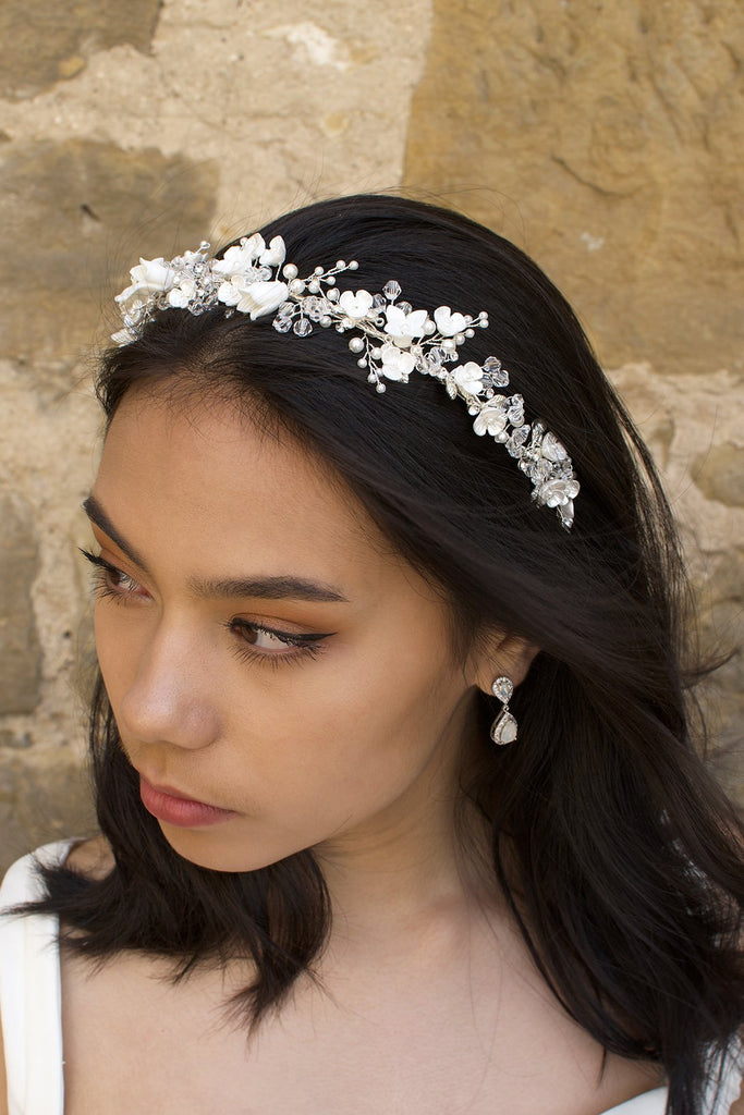 A bride with black hair wears a headband of ceramic flowers and clear crystals with a wall background