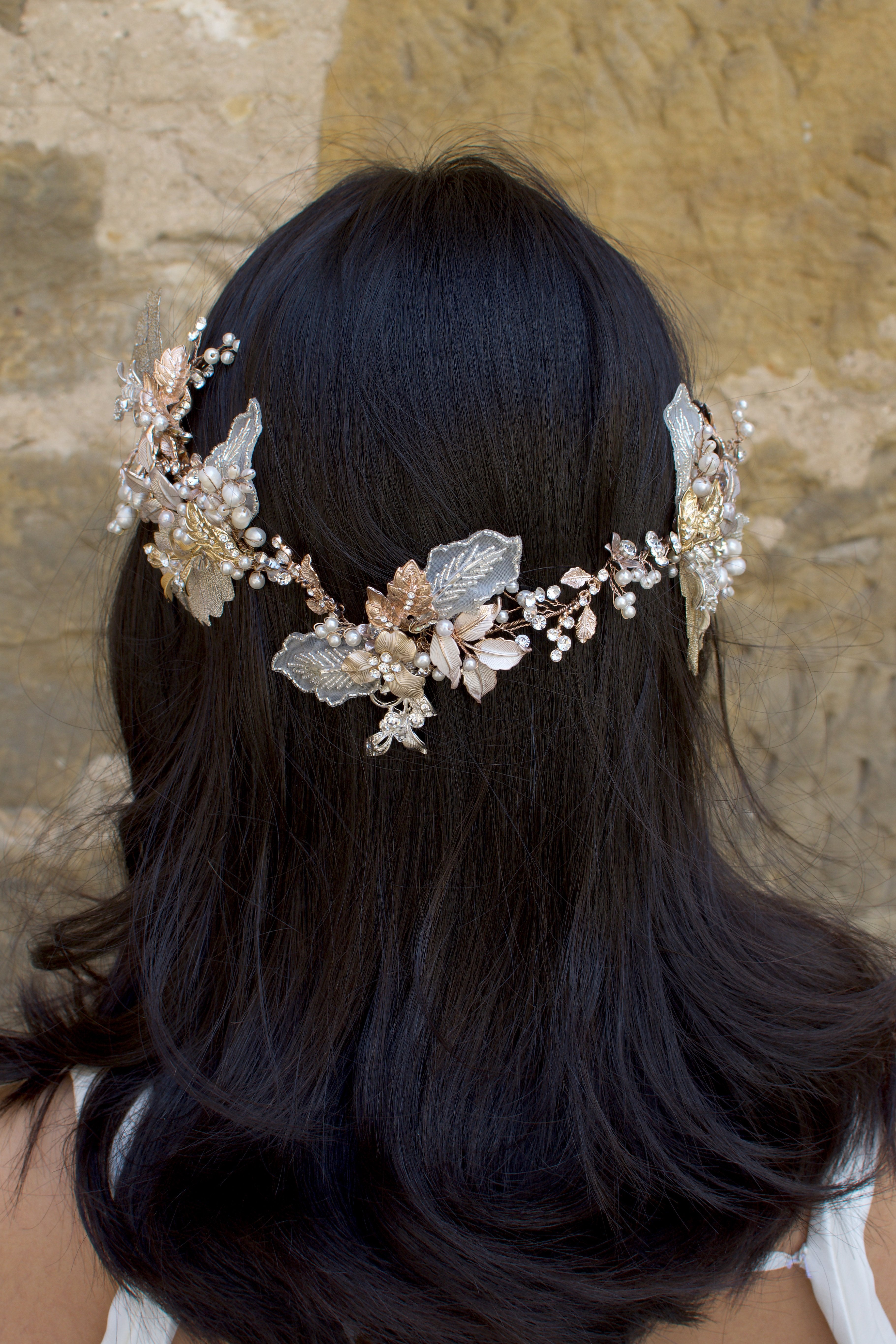 A dark haired model with hair down wears a Bridal Vine in Silver, Gold and Rose Gold with a background of a stone wall