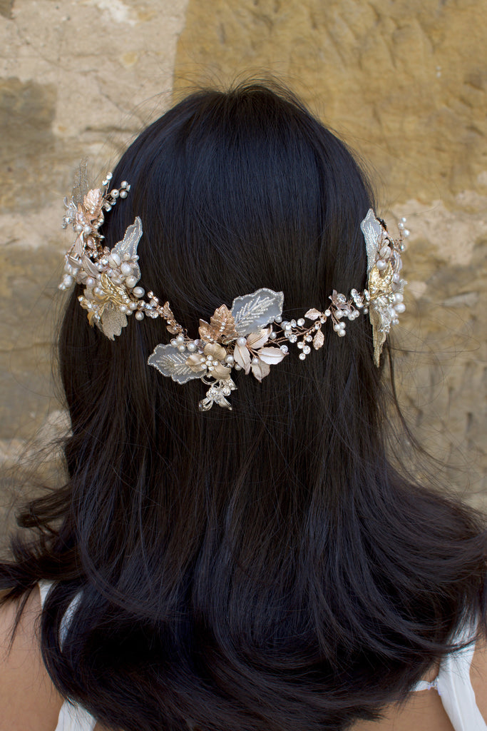 A dark haired model with hair down wears a Bridal Vine in Silver, Gold and Rose Gold with a background of a stone wall