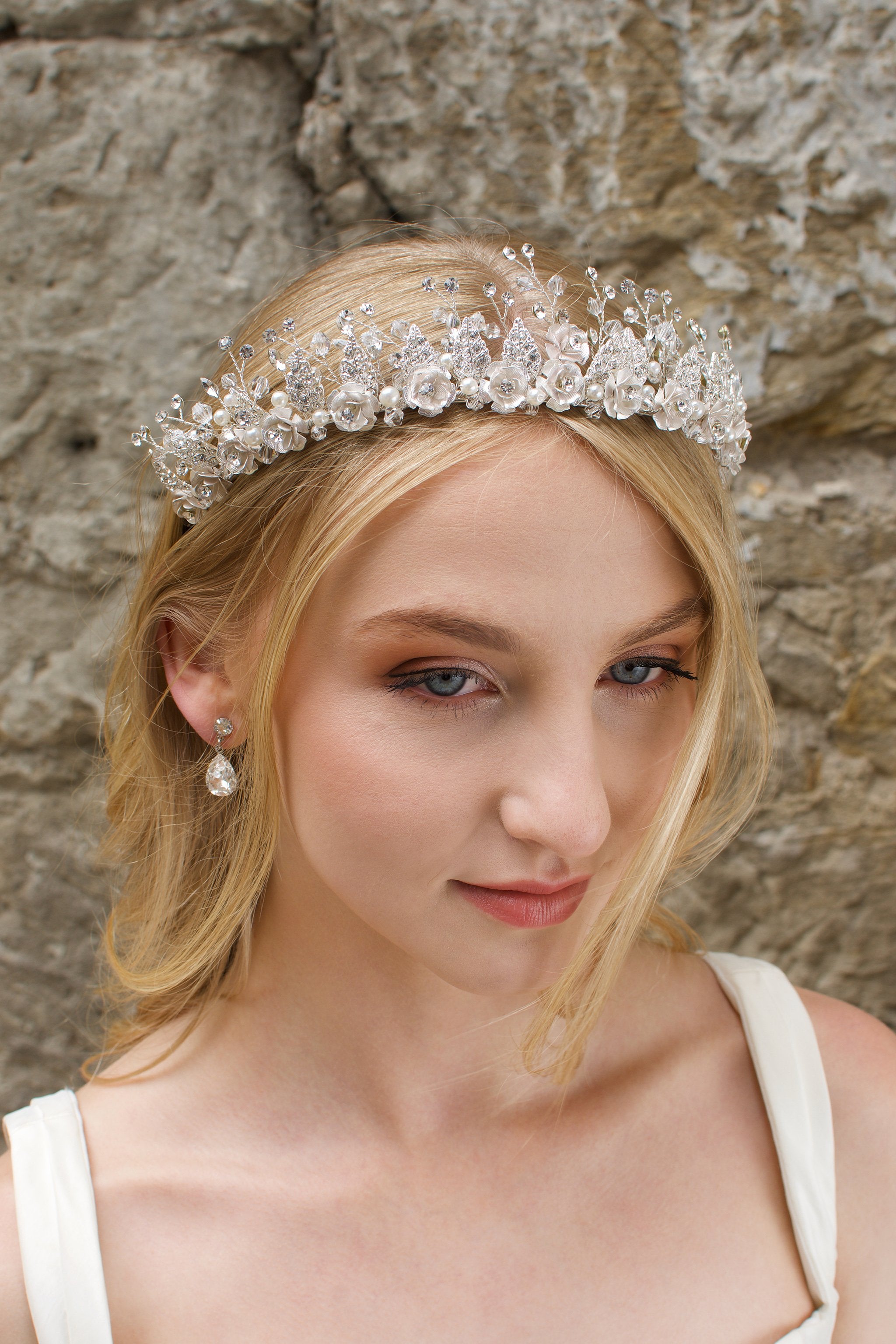 A Silver Flowers and pearls wide tiara worn by a blonde bride with a stone wall background.