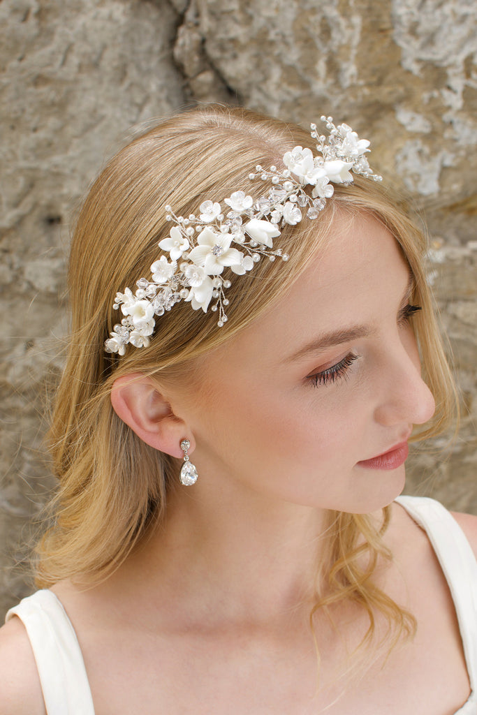 A blonde Bride wears a headband of ceramic flowers and pearls with a stone wall background
