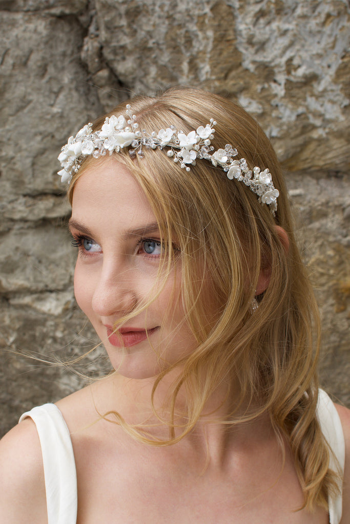 Smiling Blonde Bride wears a headband of ceramic flowers with a stone wall background