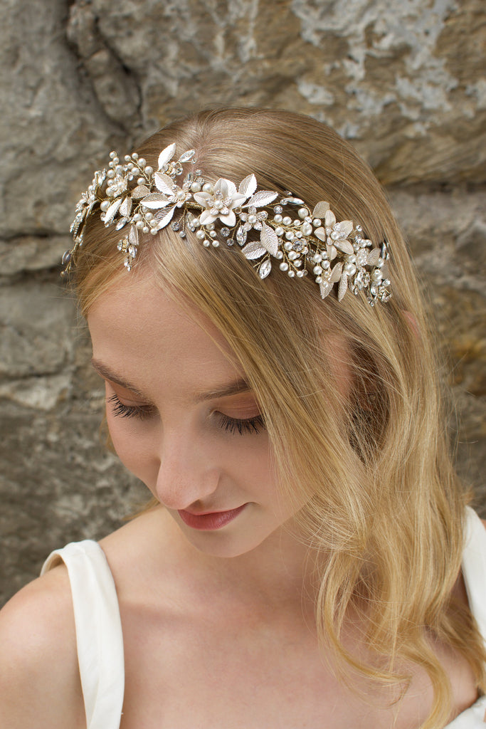 Blonde model wears a very pale gold bridal headband with a stone wall background