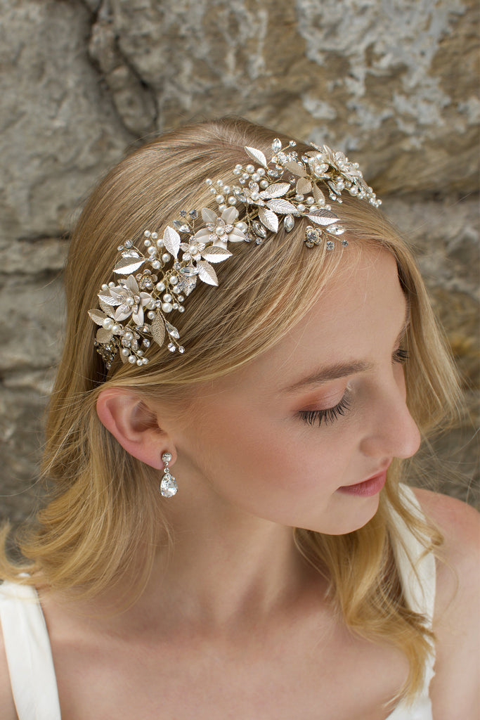 Blonde hair Bride wears a Champagne Gold wide bridal headband with leaves with a stone wall background