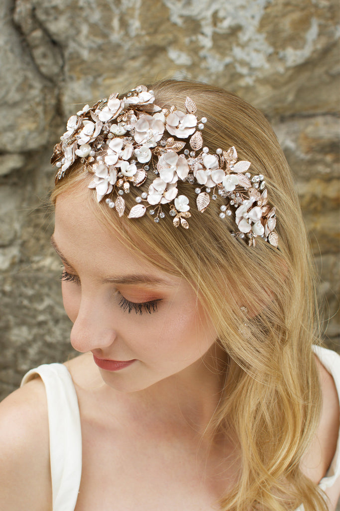 Blonde  model wears a wide headband of flowers with the background of a stone wall