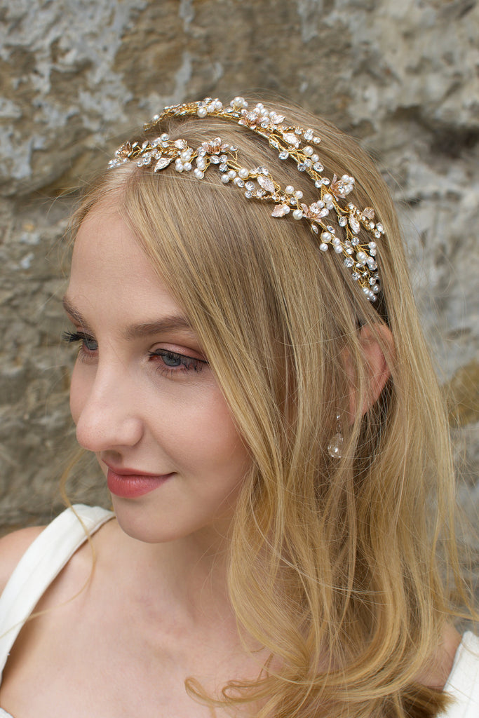 Blonde smiling bride wearing a gold and pearl headband with a stone wall backgtound