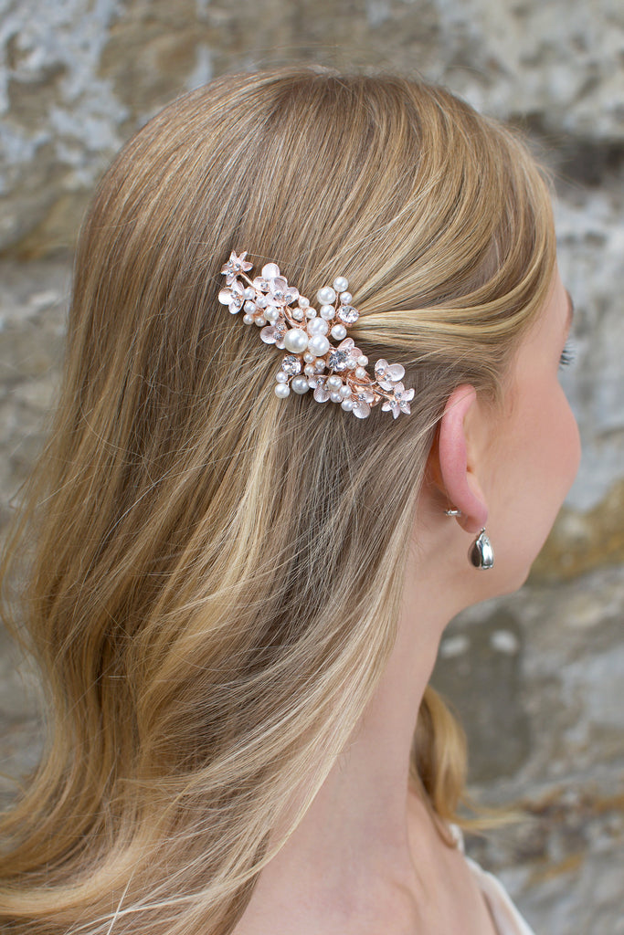 Blonde hair bride wears a pearl encrusted small side clip on rose gold with a stone wall behind.