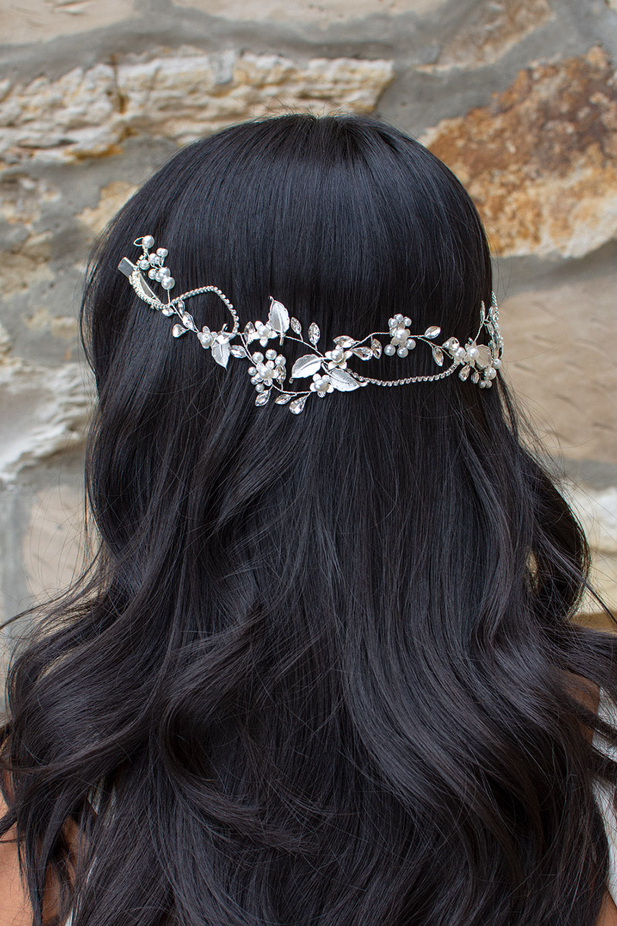 A woman with dark hair wearing a silver and pearl bridal hair vine adorned with sparkling leaves and pearl beading.