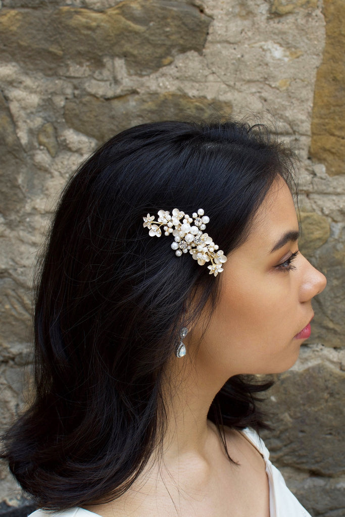 Our "Karina" Side Comb Pale Gold pearl clip worn by a model with dark hair against a stone wall
