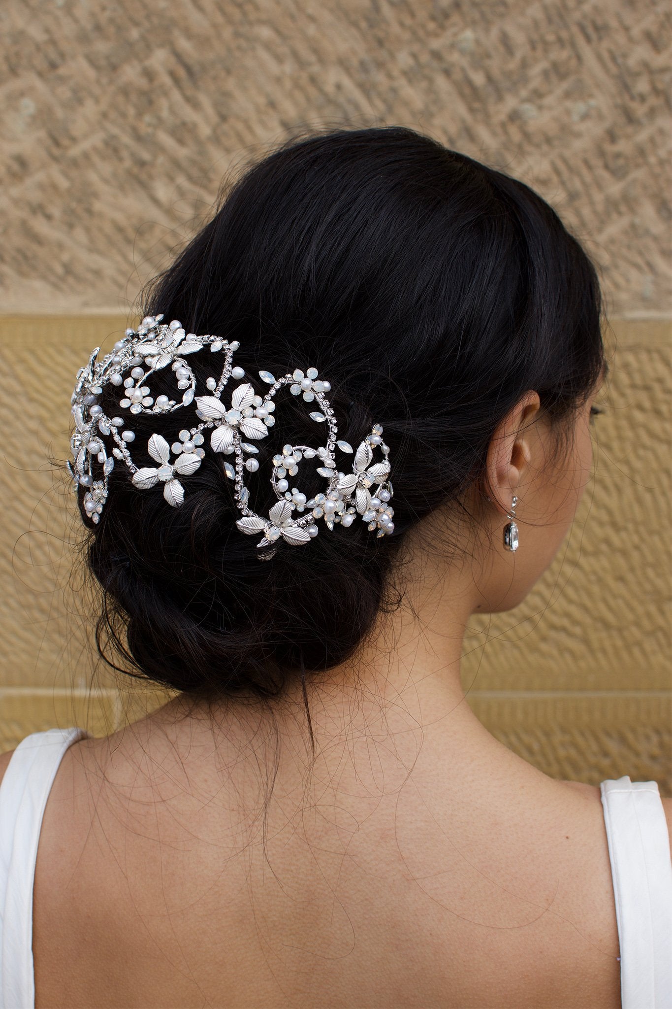 Looking right a Bridal Model wears a silver wide headband on her dark hair with a stone wall background