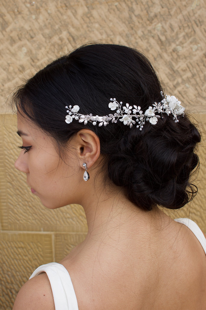 A dark haired Bride wears a porcelain flowers silver vine around the back of her head with a stone wall backdrop