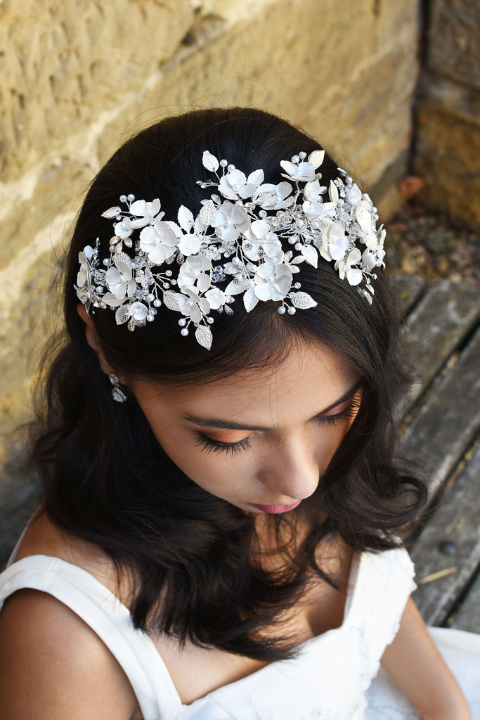 Black Haired model wears a wide headband of flowers with the background of a stone wall