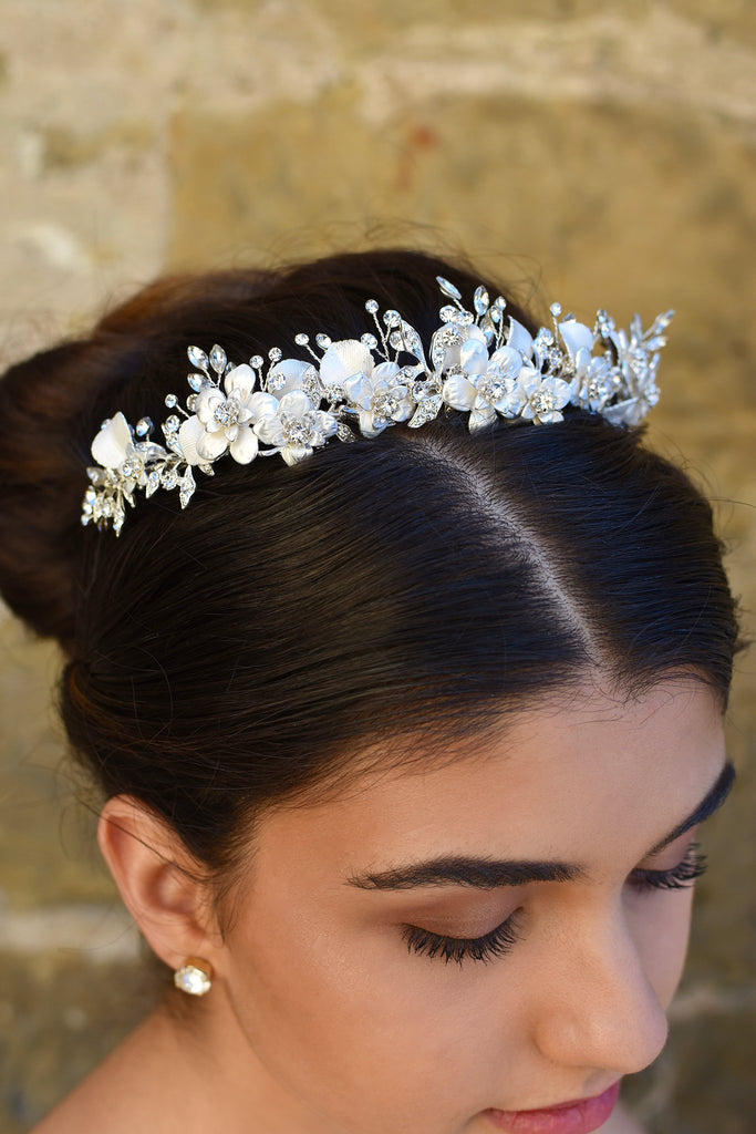 Close up of a white and silver bridal tiara with flowers and leaves worn by a dark hair model with her hair up