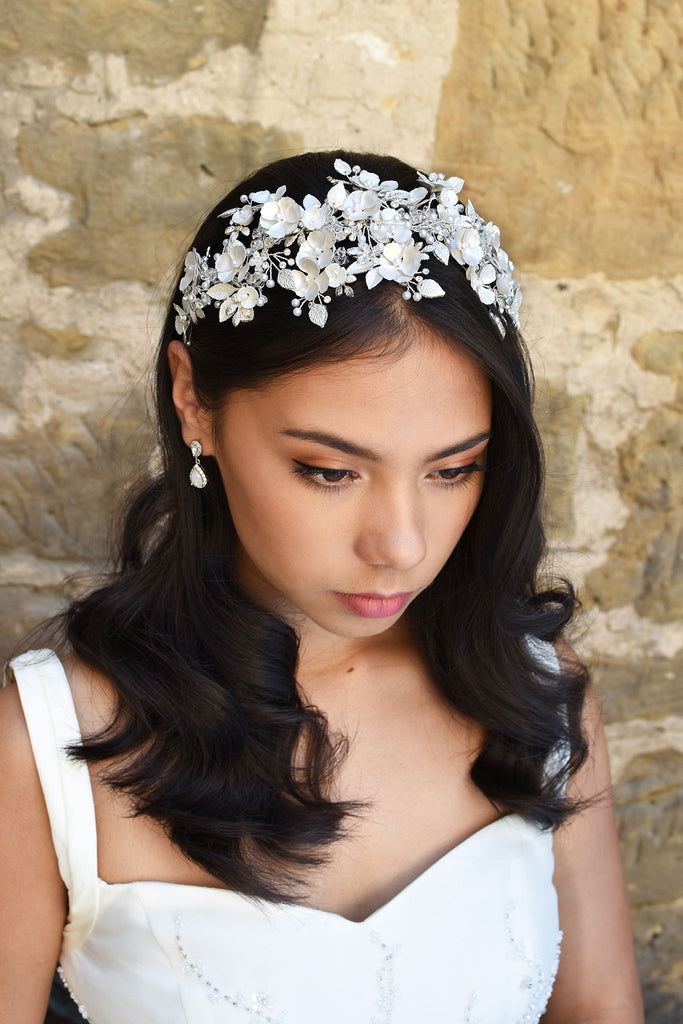 Dark Haired model wears a wide headband of flowers with the background of a stone wall