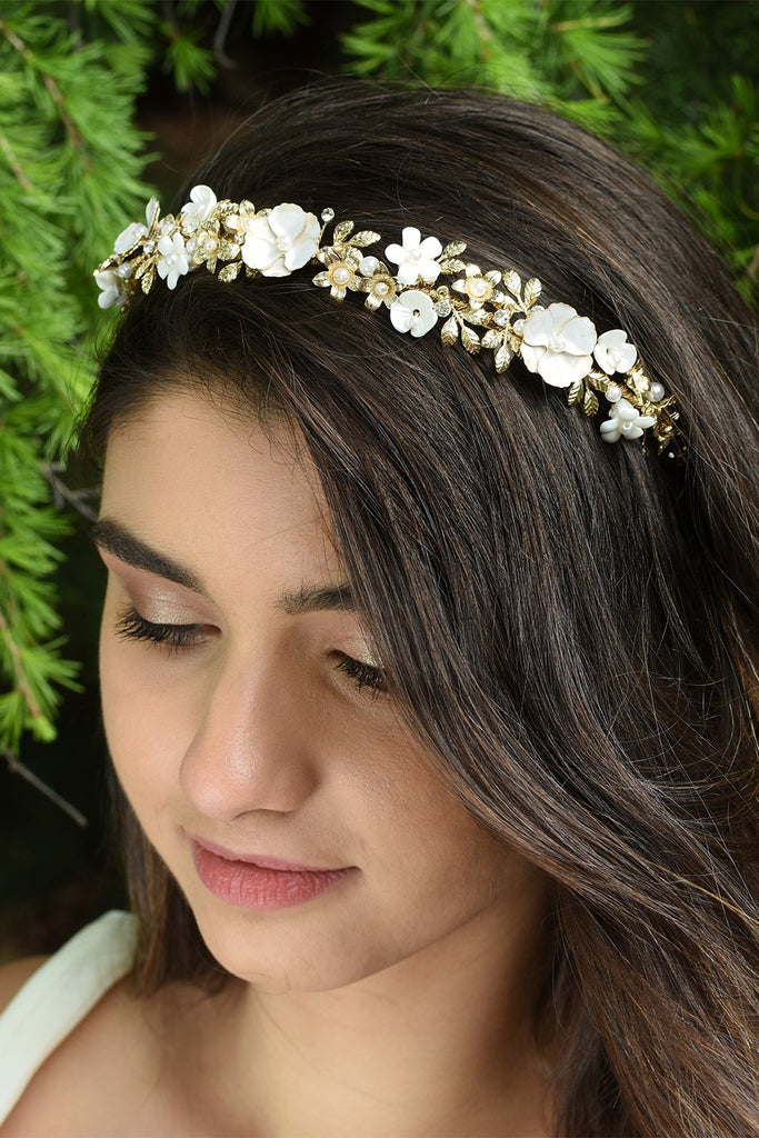 Smiling Dark hair Bridal Model wearing Flower and gold headband with green pine tree background