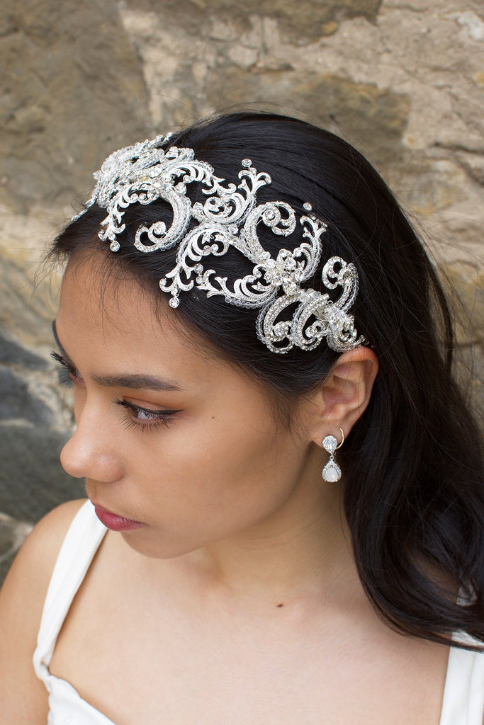 Wide Silver and clear crystal bridal headband worn by a dark haired bride with a stone backdrop
