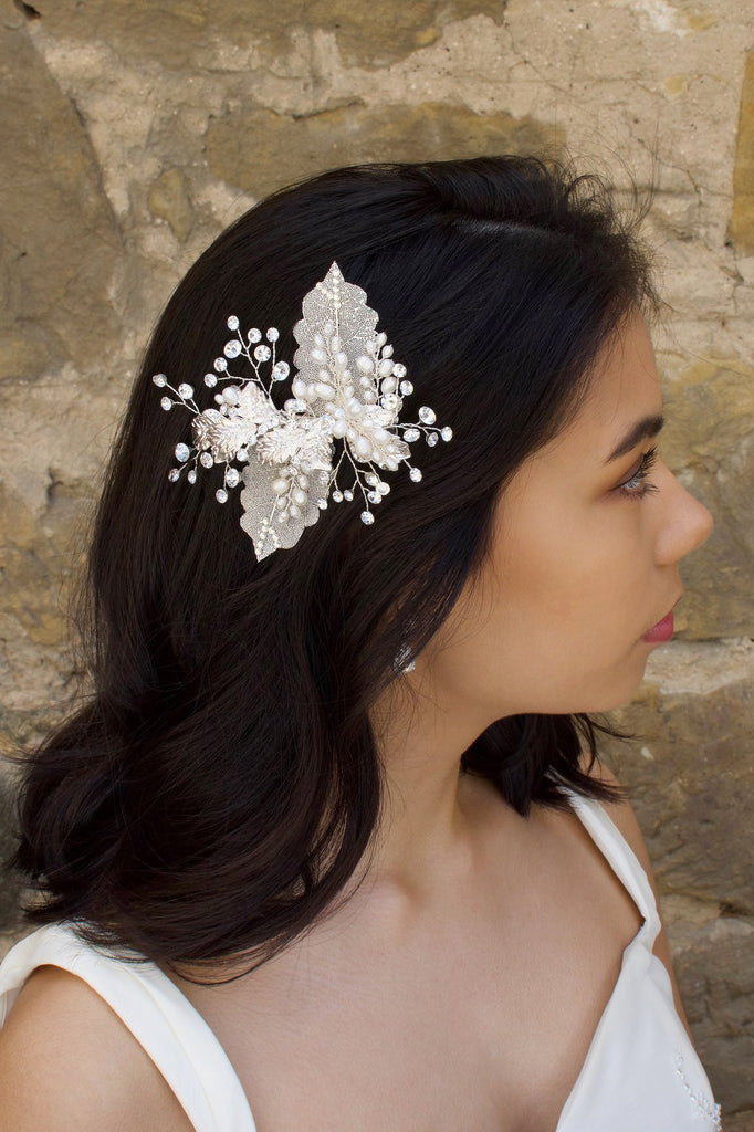 Dark hair bride wears a filigree leaf silver side comb with pearls in front of an old stone wall