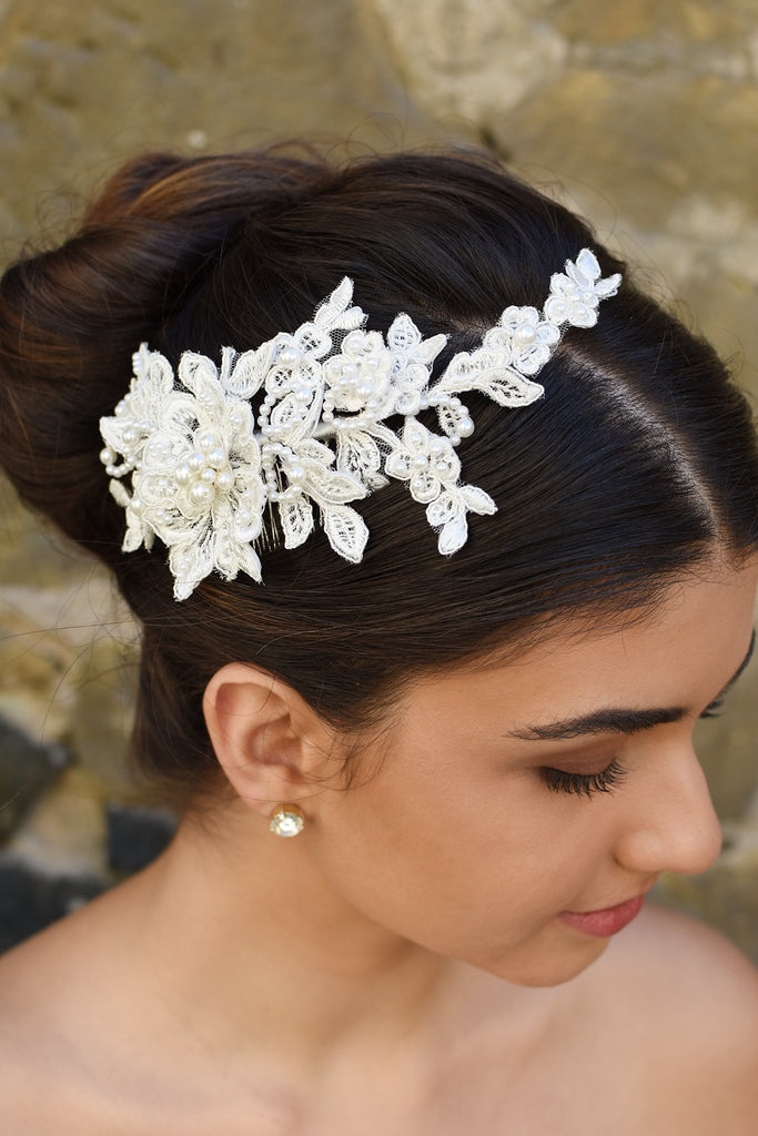 Lace side comb with pearls worn by a dark hair model in front of a stone wall.