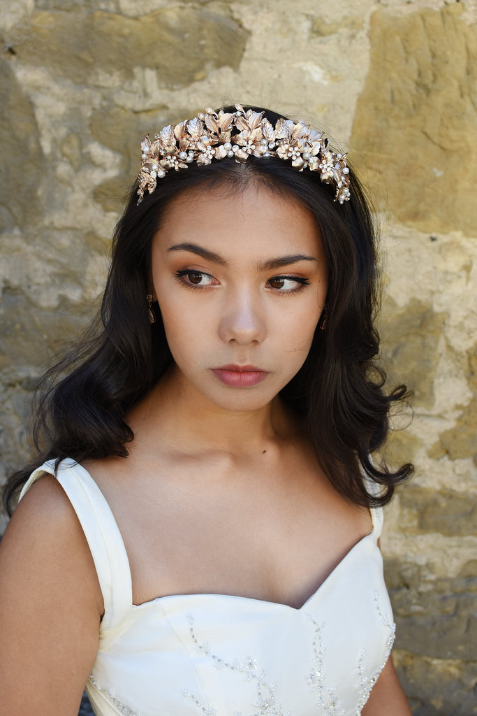 Bridal Model wears a pale rose gold tiara in her dark hair standing against an old stone wall