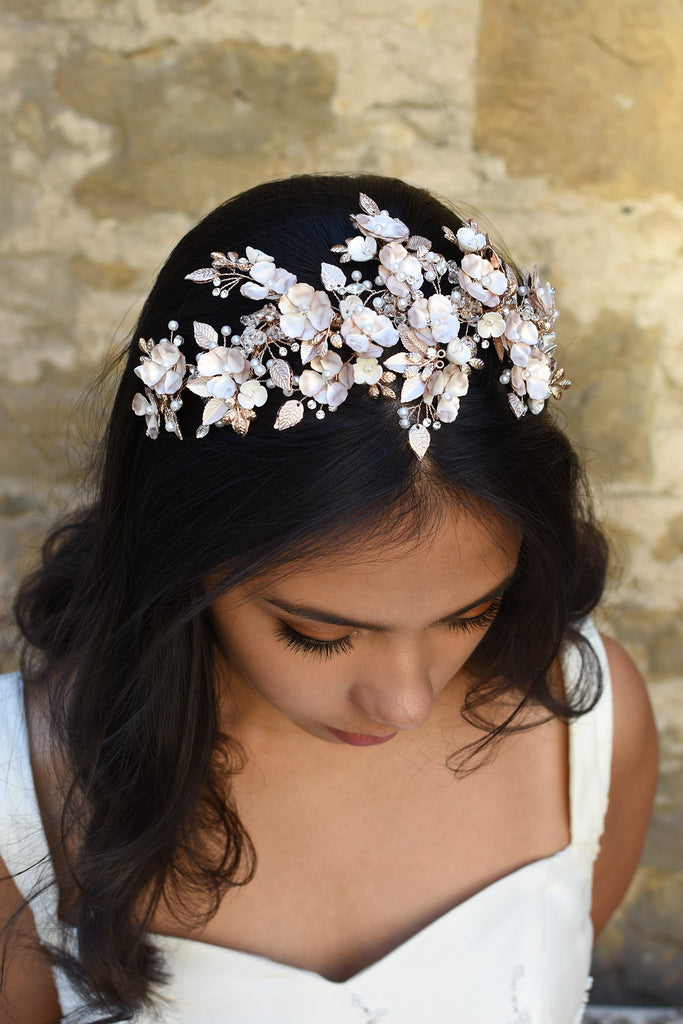 Dark Haired model wears a a pale rose gold wide headband of flowers with the background of a stone wall