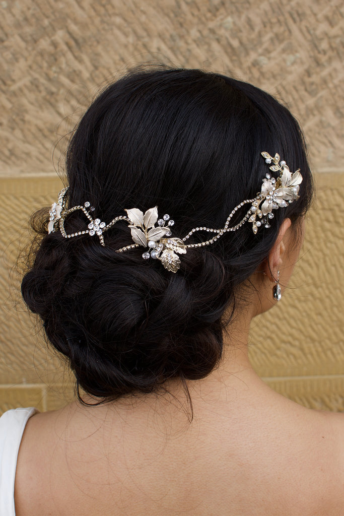 A dark haired model with curly hair wears a pale gold bridal vine at the back of her head 
