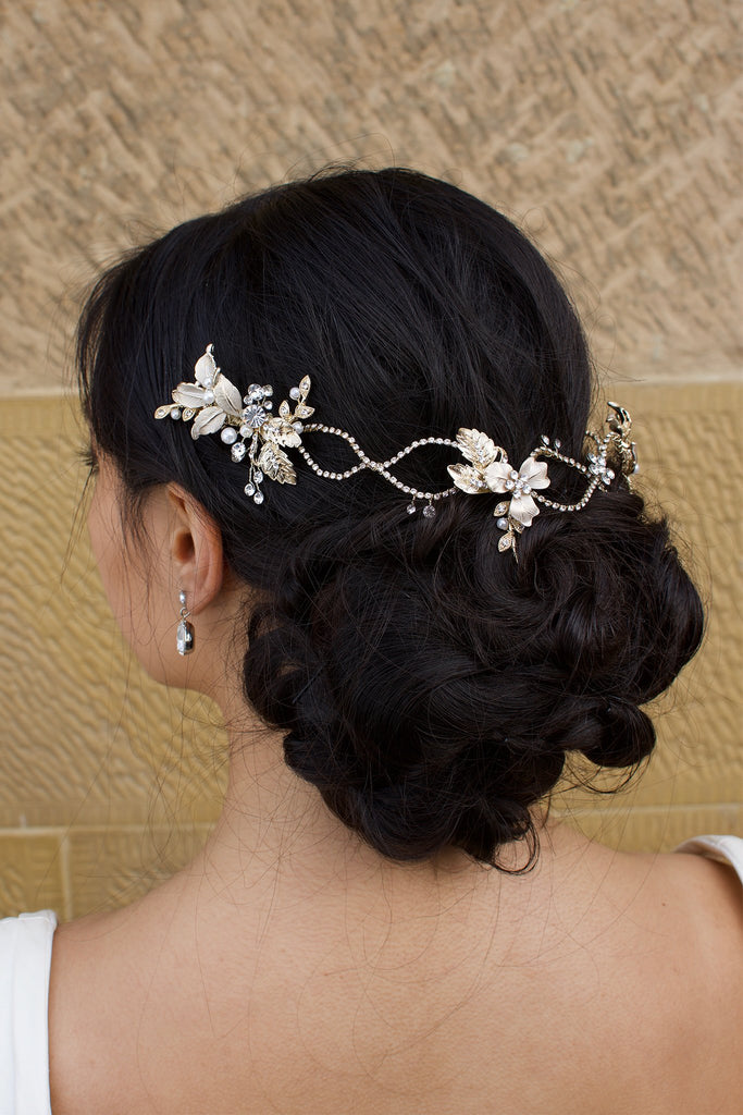 A dark haired model with curly hair wears a pale gold  vine at the back of her head